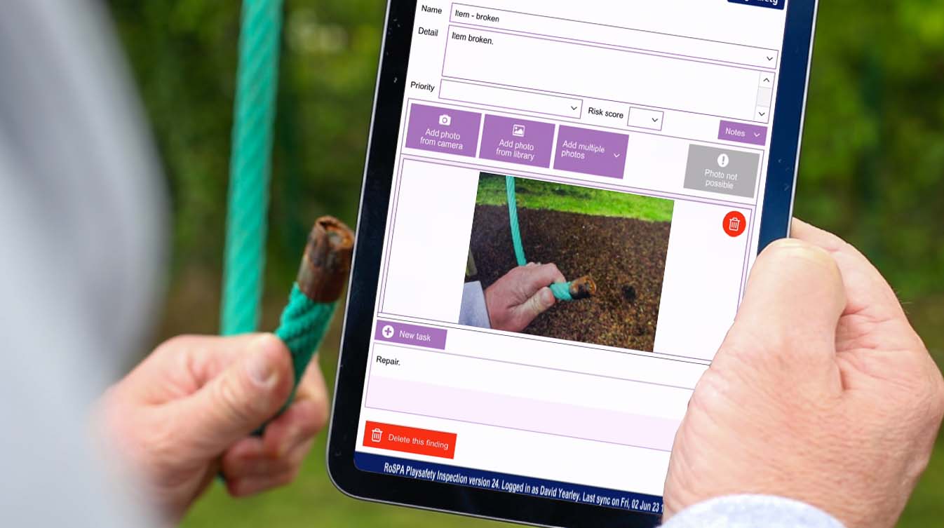 A playground inspector takes a photograph of some faulty play equipment and looks at it on a tablet screen